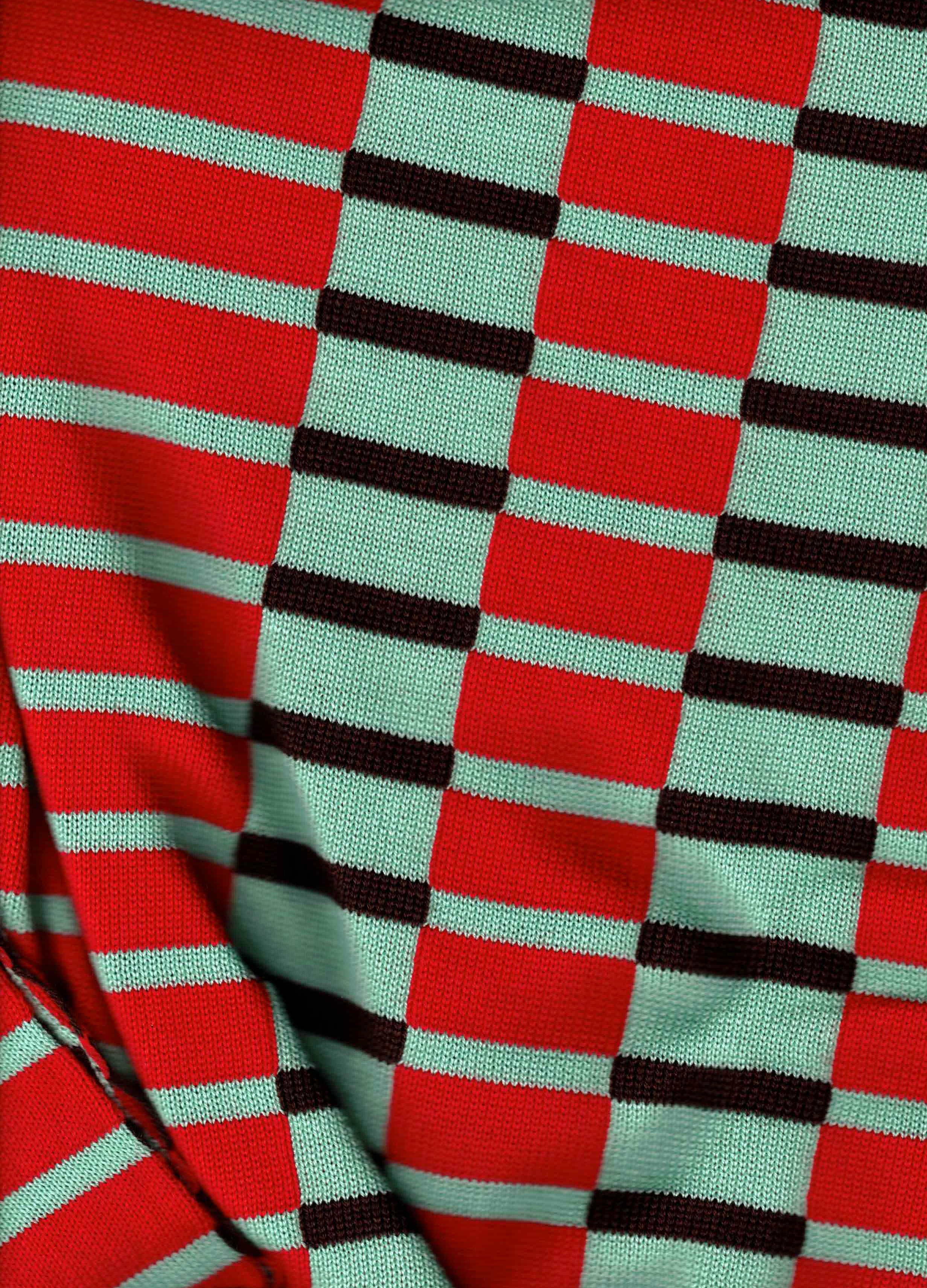 A close-up of a knit fabric with a geometric pattern of red, mint green, and black stripes and squares.