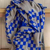 The WAVE blanket in CURIO’s signature balanced chain check is knitted from the finest Merino wool yarn (21 microns) for unparalleled softness and durability. Blanket edges are finished by hand, and the CURIO label affixed to each blanket is embroidered in Central Victoria from Australian cotton and attached by hand.. The blanket is Bright blue with checked pattern throughout and a mushroom base colour
