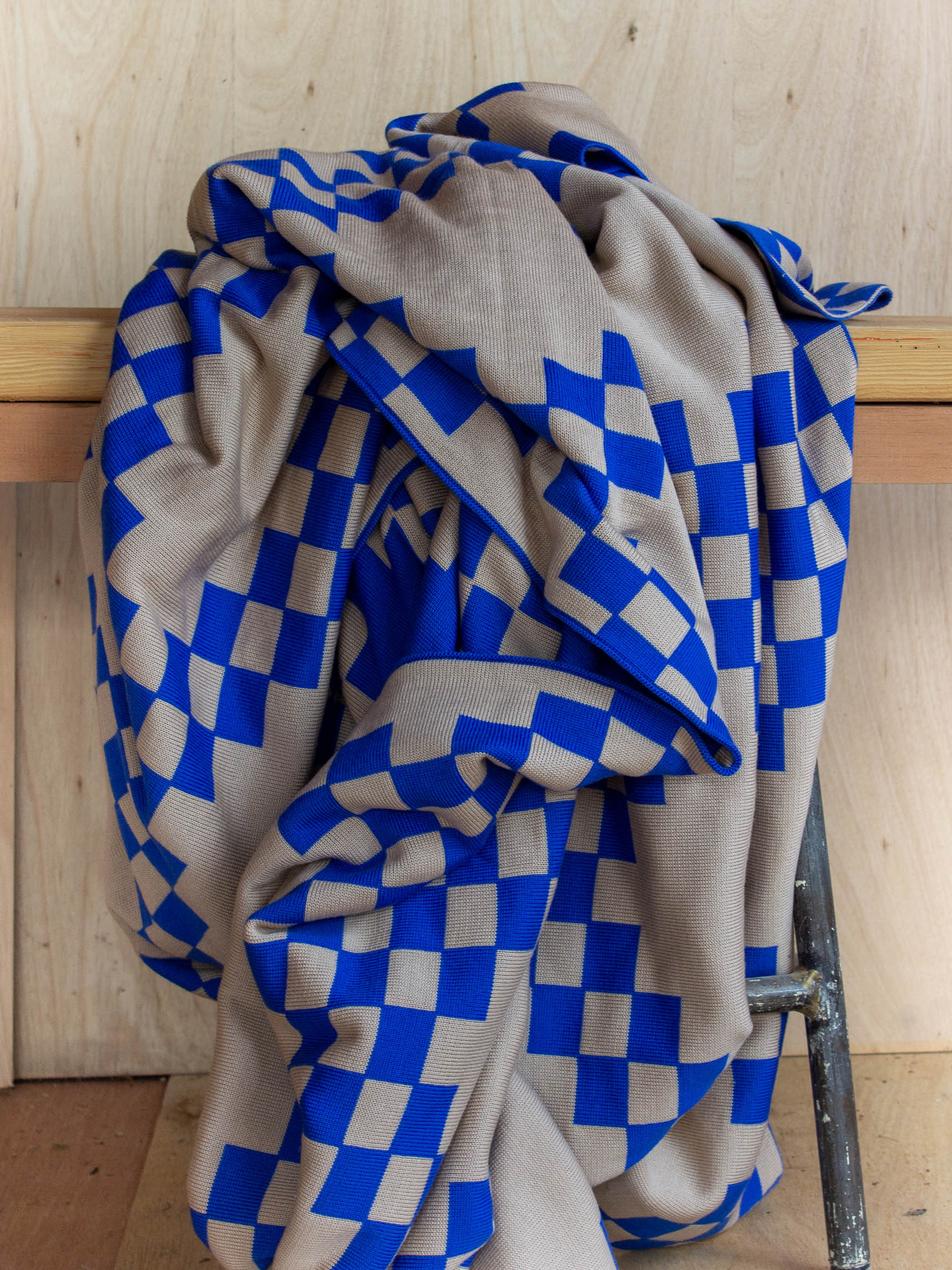 The WAVE blanket in CURIO’s signature balanced chain check is knitted from the finest Merino wool yarn (21 microns) for unparalleled softness and durability. Blanket edges are finished by hand, and the CURIO label affixed to each blanket is embroidered in Central Victoria from Australian cotton and attached by hand.. The blanket is Bright blue with checked pattern throughout and a mushroom base colour