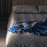 The WAVE blanket in CURIO’s signature balanced chain check is knitted from the finest Merino wool yarn (21 microns) for unparalleled softness and durability. Blanket edges are finished by hand, and the CURIO label affixed to each blanket is embroidered in Central Victoria from Australian cotton and attached by hand.. The blanket is Bright blue with checked pattern throughout and a mushroom base colour